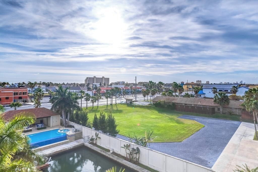 A residential area with a swimming pool, a grassy lawn, and a view of distant buildings.