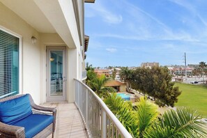 Varanda com sofá de vime, porta de vidro e vista para uma piscina e edifícios.