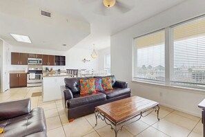 A modern living room with a sofa, coffee table, and a view of the kitchen. - Las Marinas Condominiums 405 (South Padre Island)