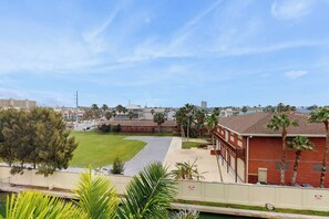 A view of a building with a parking lot, a grassy area, and palm trees. - Las Marinas Condominiums 405 (South Padre Island)