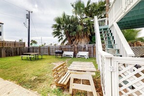 Ein Garten mit einer Holzterrasse, einem Picknicktisch und einem Grill.