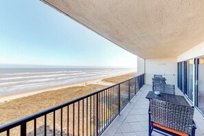 A balcony with a view of the beach, featuring a railing, two wicker tables, and a bench. - Ocean Vista Condominiums #1004 (South Padre Island)