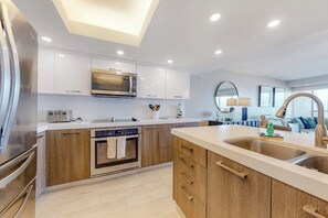 Une cuisine moderne avec des meubles blancs, un four à micro-ondes, un lave-vaisselle et un grand îlot central doté d’un évier.