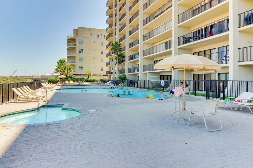 Un espace piscine d’hôtel comprenant plusieurs piscines, des chaises longues et un bâtiment doté de balcons.