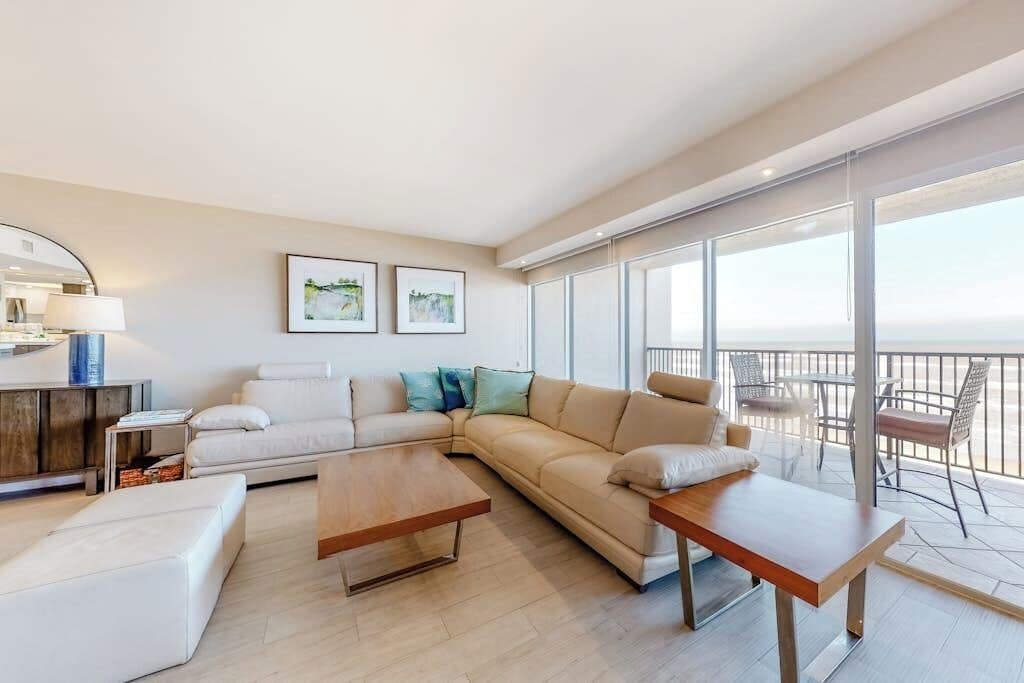 Un salon moderne avec un canapé, une table basse et un balcon aménagé avec du mobilier d’extérieur.