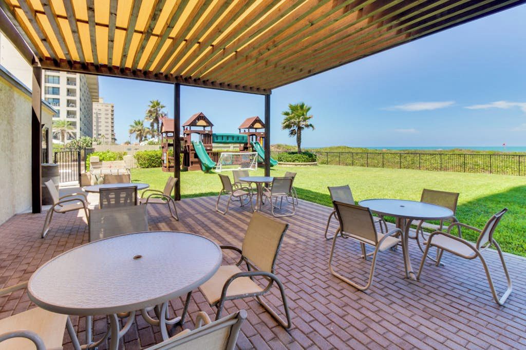 An outdoor patio with tables and chairs, a children's play area, and a view of the ocean.
