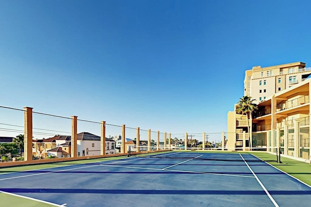 Ein Tennisplatz im Freien mit blauem Himmel, umgeben von Wohnhäusern.