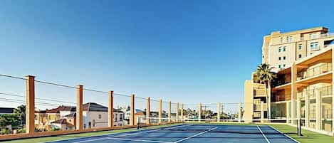 Ein Tennisplatz im Freien mit blauem Himmel, umgeben von Wohnhäusern.