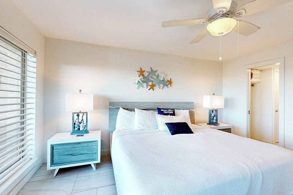 A bedroom with a bed, nightstands, a ceiling fan, and a wall decoration.