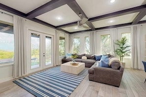 A spacious living room with a sectional sofa, a coffee table, and large windows offering a view of the outdoors. - Casa Sol Y Mar - Private Pool, Steps to the Sand (Port Isabel)