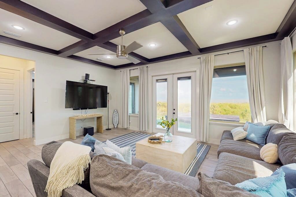A modern living room with a flat-screen TV, a ceiling fan, and a large window with curtains.