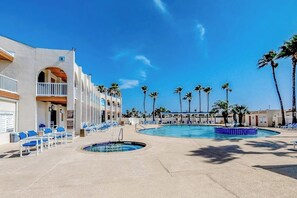 A hotel pool area with multiple lounge chairs, a small pool, and palm trees. - Long Island Village 349 Sand Dollar (Port Isabel)