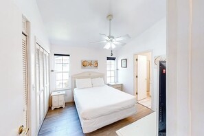Un dormitorio con cama, ventilador de techo, mesita de noche y puerta que da a otra habitación.