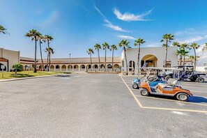 Un estacionamiento con un carrito de golf, palmeras y un edificio con ventanas arqueadas.