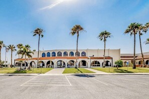 A building with multiple arched entrances, a parking lot, and palm trees. - Long Island Village 349 Sand Dollar (Port Isabel)