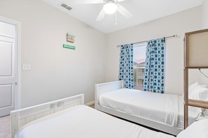 A bedroom with two beds, a ceiling fan, and a window with patterned curtains. - Las Joyas Bayview Home #216 (Port Isabel)