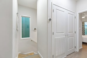 A hallway with white walls, a window with blue shutters, a door with a vent, and a staircase leading to another room. - Las Joyas Bayview Home #216 (Port Isabel)