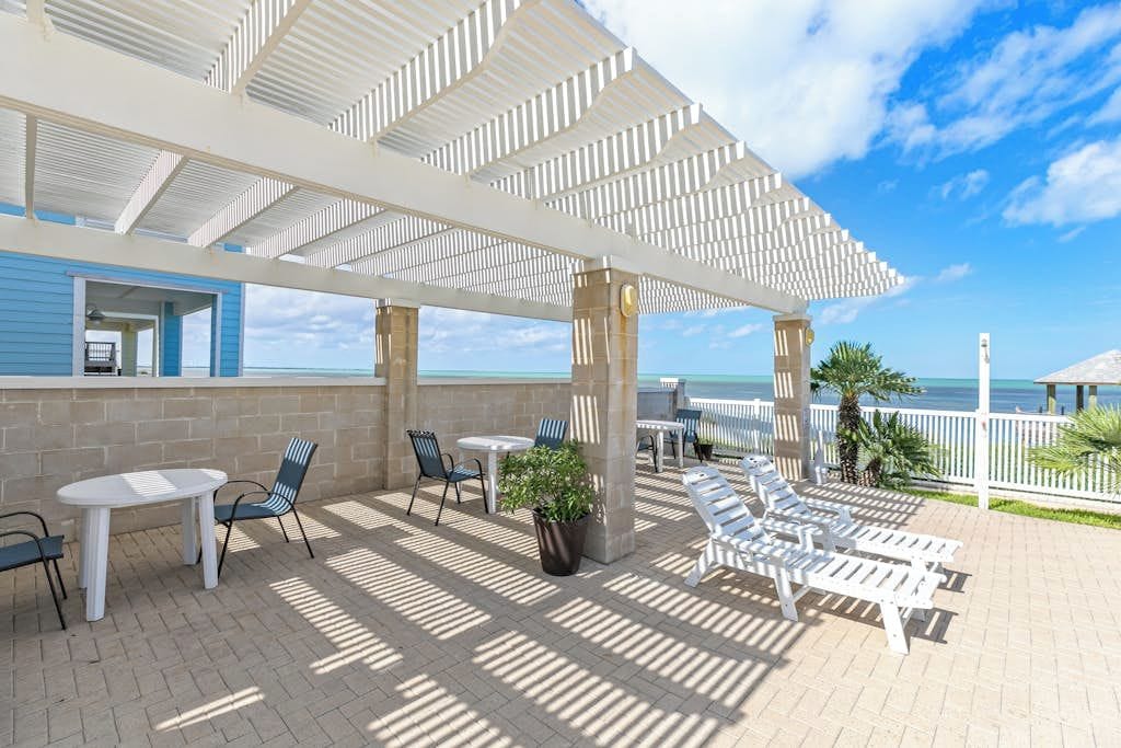 A covered outdoor area with tables and chairs, a view of the ocean, and a building with a blue exterior.