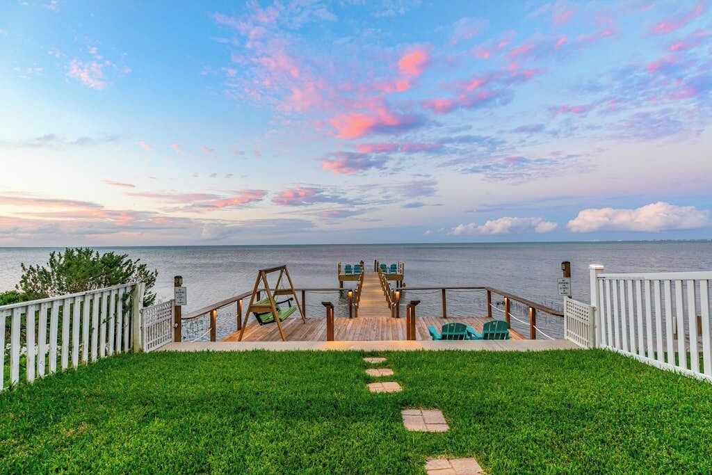 Une terrasse en bois avec vue sur la mer, une pelouse et une clôture blanche.
