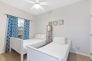 A bedroom with two beds, a ceiling fan, and a window with patterned curtains. - Las Joyas Bayview Home #216 (Port Isabel)