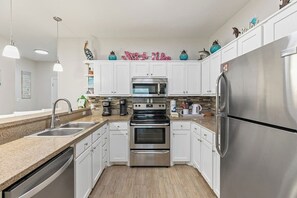 A modern kitchen with white cabinets, stainless steel appliances, and a granite countertop. - Las Joyas Bayview Home #216 (Port Isabel)