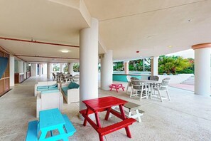 Ein Außenbereich mit weißen Korbmöbeln, roten und blauen Tischen und einem Pool im Hintergrund.