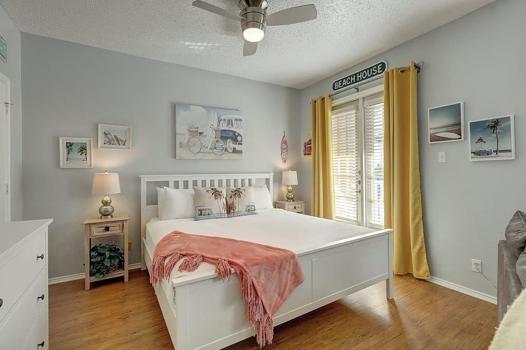Un dormitorio con cama, mesitas de noche, ventilador de techo y ventana con cortinas.