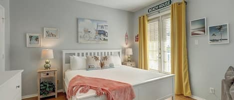Un dormitorio con cama, mesitas de noche, ventilador de techo y ventana con cortinas.