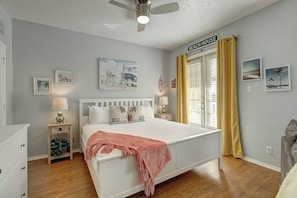 A bedroom with a bed, bedside tables, a ceiling fan, and a window with curtains. - Beach Club - Seas the Day (Corpus Christi)