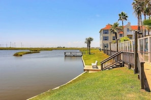 A waterfront property with a dock, a grassy area, and a building with balconies. - Beach Club - Seas the Day (Corpus Christi)