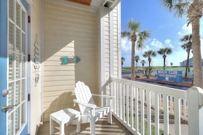 A porch with a white chair and table, a sign reading 'Beach Club Private Residences,' and palm trees in the background. - Beach Club - Seas the Day (Corpus Christi)