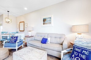 A living room with a sofa, a coffee table, and a dining area with chairs and a table. - Beach Club 173 & 174 (Corpus Christi)