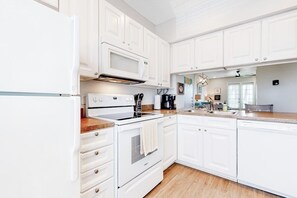 A kitchen with white cabinetry, a microwave, stove, and a coffee maker. - Beach Club 173 & 174 (Corpus Christi)