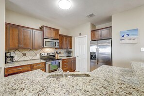 A kitchen with wooden cabinets, a stainless steel refrigerator, a microwave, and a granite countertop. - Texas Two Steps From Beach (Corpus Christi)