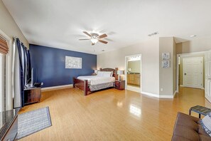 A bedroom with a bed, bedside tables, a ceiling fan, and a view into the adjacent bathroom. - Texas Two Steps From Beach (Corpus Christi)