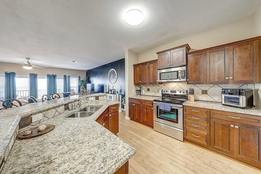 A kitchen with granite countertops, wooden cabinets, a microwave, oven, and a dining area with a chandelier.