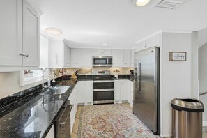 A modern kitchen with white cabinets, stainless steel appliances, and a black granite countertop. - Gulf Beach House #10 (Port Aransas)