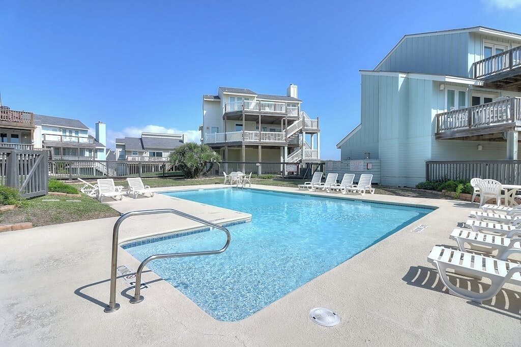 A swimming pool with lounge chairs and a building with multiple balconies.