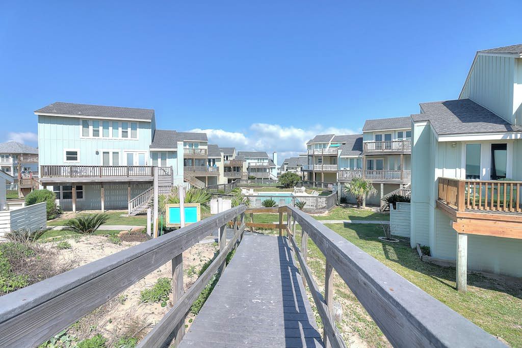 A coastal residential area with multiple two-story houses, a wooden walkway, and a small pool.