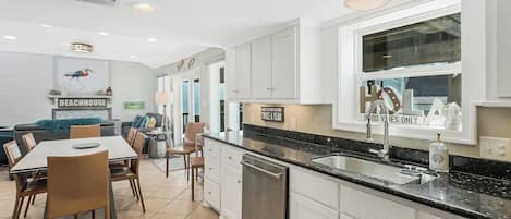 A modern kitchen with white cabinetry, a black countertop, and a dining area with a table and chairs.