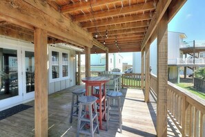 A covered outdoor deck with wooden beams, a table with chairs, and a view of a residential area. - Gulf Beach House #10 (Port Aransas)
