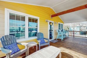 Une véranda couverte avec des fauteuils Adirondack et une table, un revêtement extérieur jaune et une terrasse en bois.