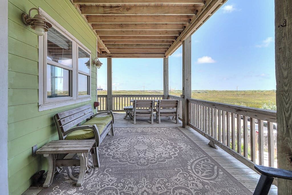 A covered porch with a patterned rug, wooden benches, and a view of the landscape.
