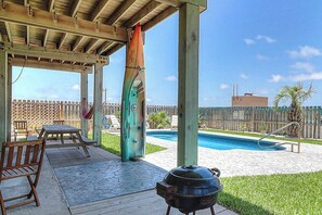 An outdoor patio with a barbecue grill, pool, and wooden deck furniture. - Gulf Breezes Unit A - Gulf Views & Pool, Dogs OK (Port Aransas)