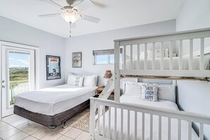 A bedroom with a bed, a white crib, a ceiling fan, and a window with a view. - Gulf Breezes Unit A - Gulf Views & Pool, Dogs OK (Port Aransas)
