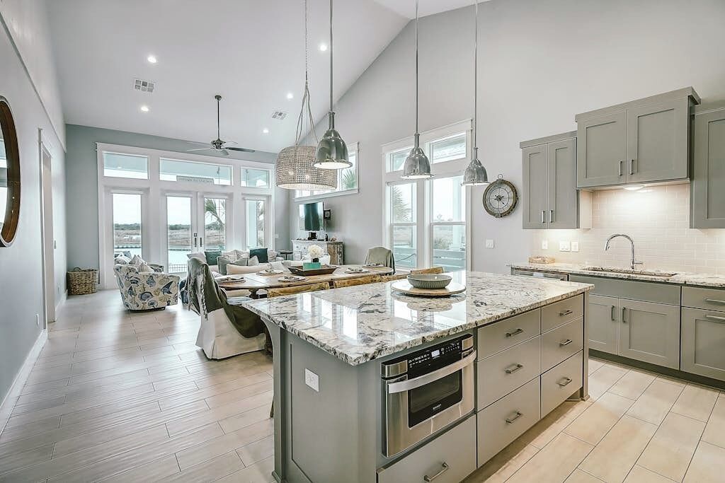 A modern kitchen with a large island, pendant lighting, and a view to the living area.
