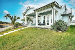 A two-story house with a covered porch, a well-maintained lawn, and a small garden area with plants. - Reserve at St Charles Bay - Cottage By The Sea (Rockport)