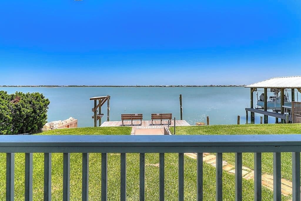 A deck with a view of a calm lake, wooden benches, and a covered area with a railing.