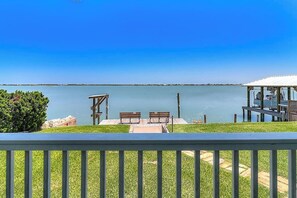 A deck with a view of a calm lake, wooden benches, and a covered area with a railing. - The Cottage on Salt Lake (Rockport)