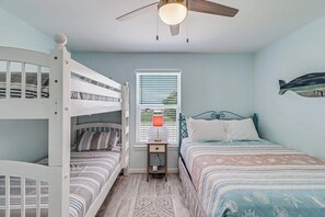 Une chambre avec des lits superposés, un lit simple, un ventilateur de plafond, une fenêtre avec des stores et une décoration murale représentant des poissons.
